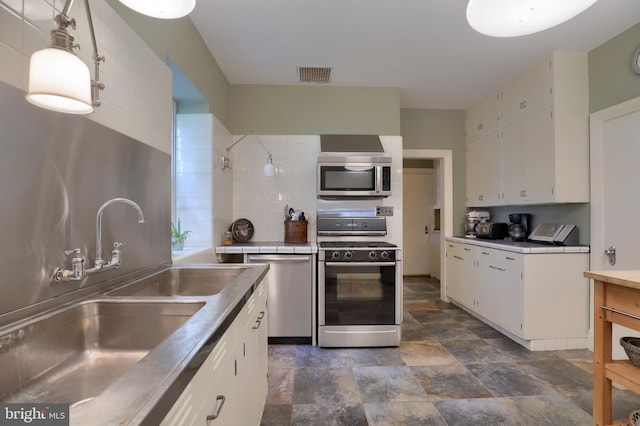 kitchen with visible vents, a sink, stainless steel appliances, tile counters, and white cabinetry