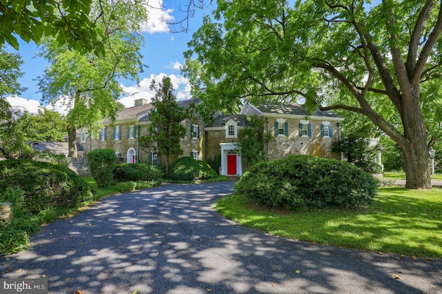 view of front of home featuring aphalt driveway, a chimney, stone siding, and a front lawn