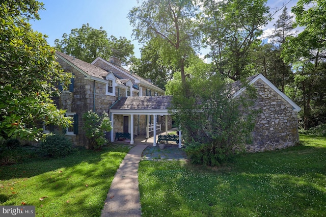 back of house with a yard, stone siding, and a chimney