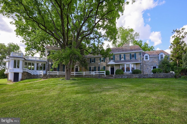 view of front facade with stone siding, a chimney, a front lawn, and fence