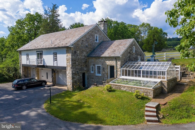 view of front of property with a greenhouse, a high end roof, a chimney, and aphalt driveway