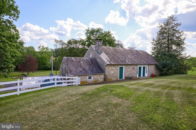 view of front facade with a front yard, a high end roof, fence, and a chimney