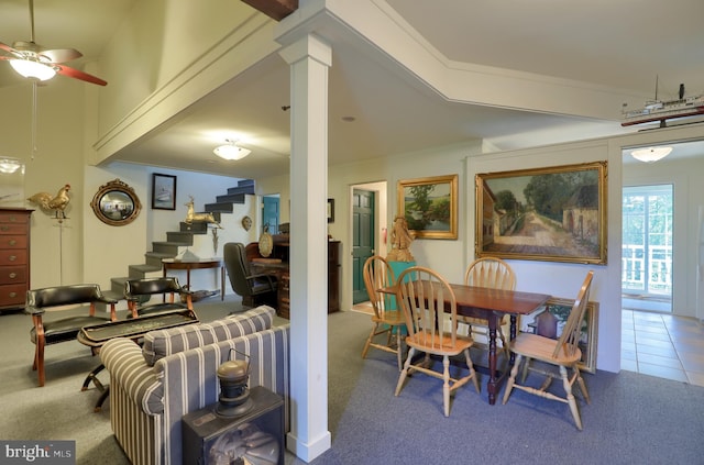 carpeted dining room featuring tile patterned floors, ornamental molding, stairway, ceiling fan, and ornate columns