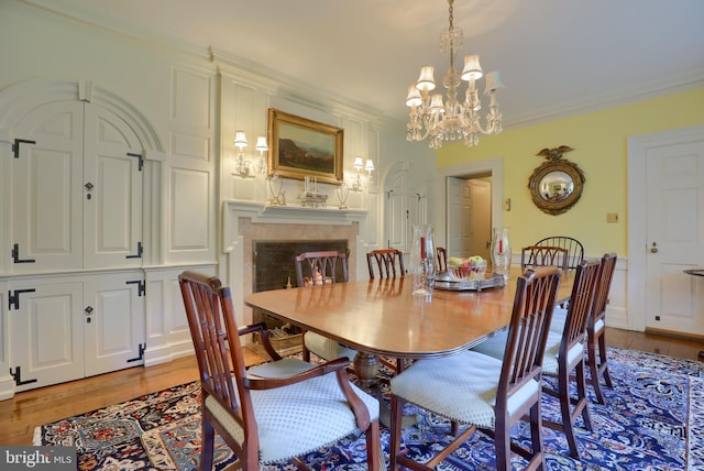 dining room featuring crown molding, light wood-style flooring, a notable chandelier, and a high end fireplace