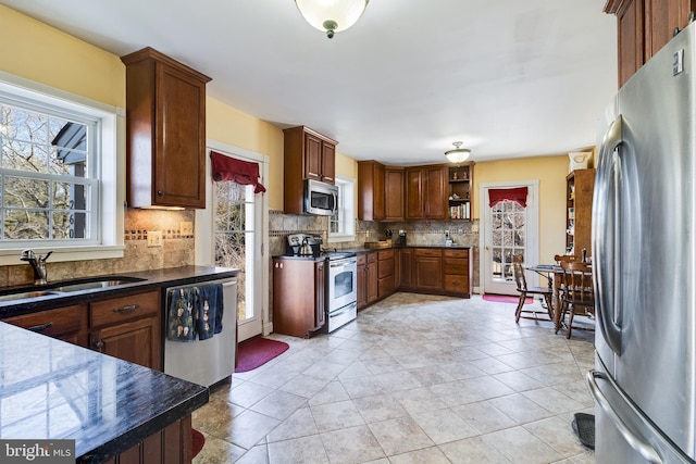 kitchen with open shelves, tasteful backsplash, dark countertops, appliances with stainless steel finishes, and a sink