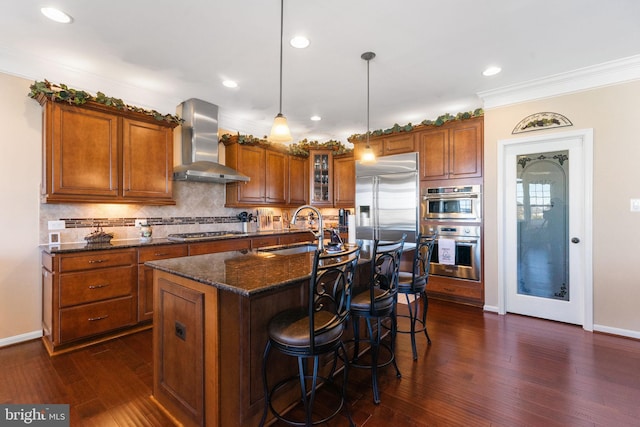 kitchen featuring brown cabinets, stainless steel appliances, tasteful backsplash, a sink, and wall chimney range hood