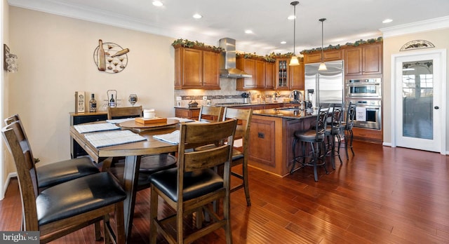 kitchen with brown cabinetry, a kitchen island with sink, stainless steel appliances, wall chimney range hood, and a sink