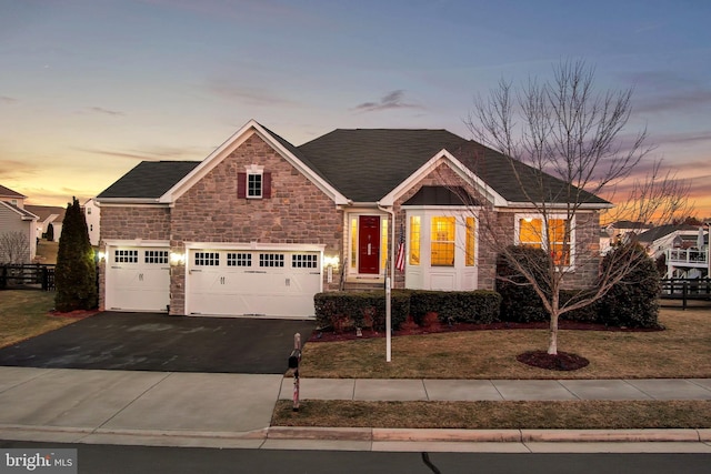 view of front facade featuring driveway, stone siding, an attached garage, and a lawn