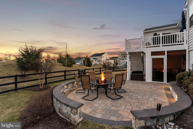 patio terrace at dusk featuring an outdoor fire pit and fence