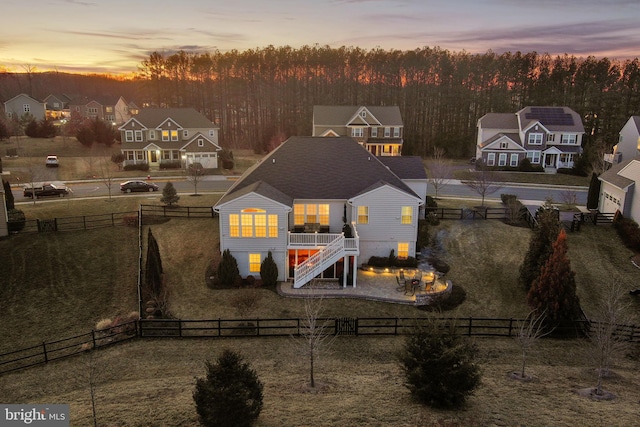 back of house at dusk featuring stairs, a patio, a lawn, and a fenced backyard