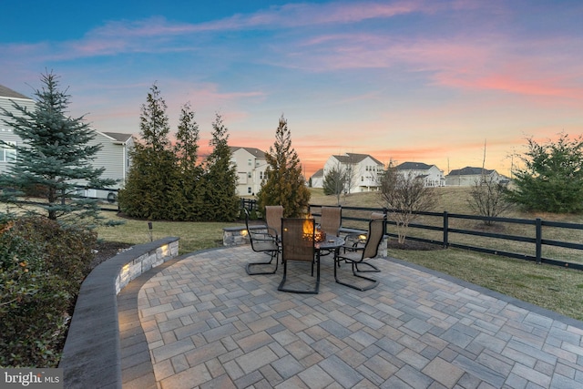 patio terrace at dusk with a residential view, outdoor dining area, and fence