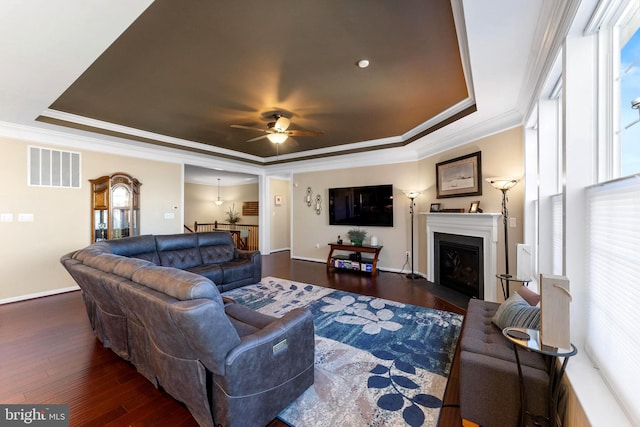 living area featuring wood finished floors, a raised ceiling, visible vents, and crown molding