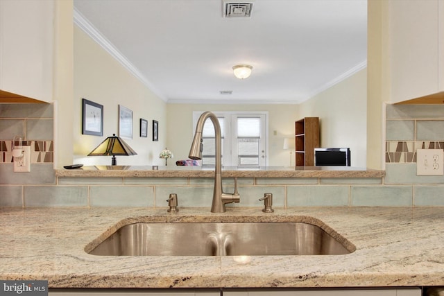 kitchen with ornamental molding, visible vents, a sink, and light stone counters