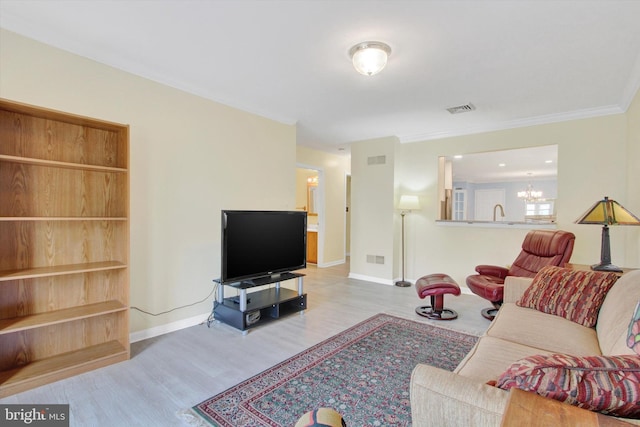 living area with a chandelier, wood finished floors, visible vents, baseboards, and ornamental molding