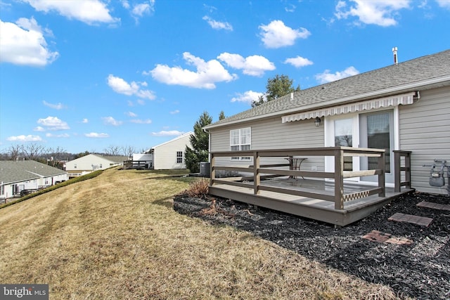 back of property with a wooden deck, a shingled roof, and a yard