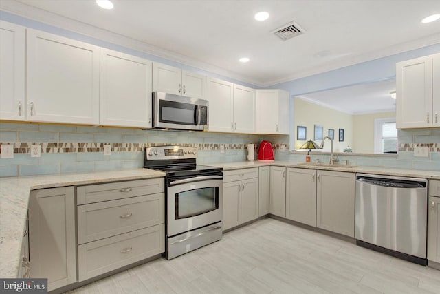 kitchen featuring a sink, visible vents, appliances with stainless steel finishes, decorative backsplash, and crown molding