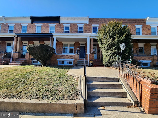 townhome / multi-family property featuring covered porch and brick siding