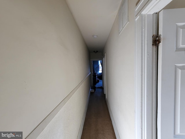 hallway featuring dark colored carpet, visible vents, and baseboards