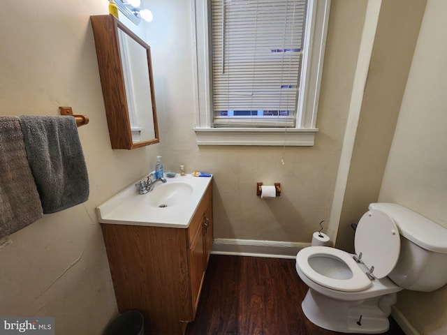 half bathroom with baseboards, vanity, toilet, and wood finished floors