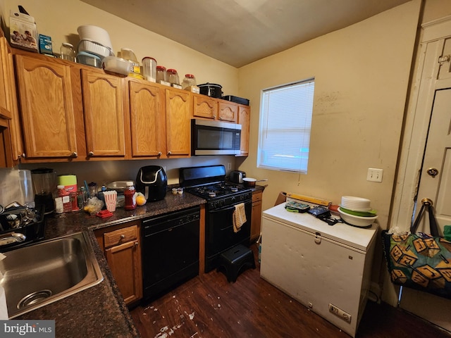 kitchen with black appliances, dark countertops, a sink, and dark wood finished floors