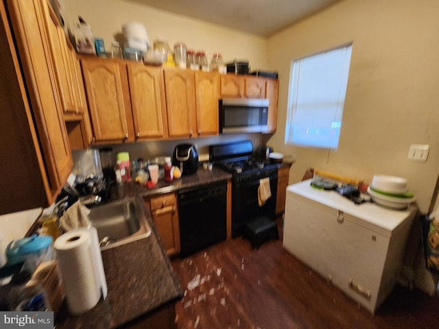 kitchen with dark countertops, black appliances, dark wood-style floors, and a sink