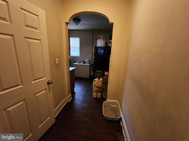 hall with baseboards, arched walkways, and dark wood-type flooring