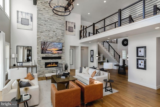 living room with a notable chandelier, a fireplace, stairway, wood finished floors, and baseboards