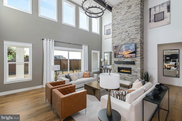 living room with a fireplace, wood finished floors, visible vents, baseboards, and an inviting chandelier