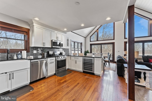 kitchen with beverage cooler, a peninsula, appliances with stainless steel finishes, white cabinetry, and dark countertops