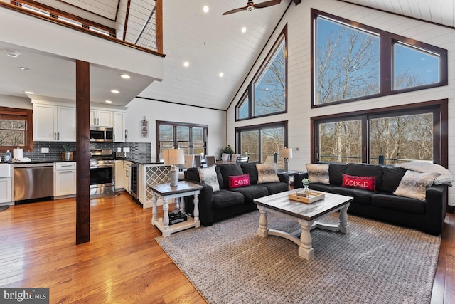 living area featuring wine cooler, light wood-type flooring, a wealth of natural light, and high vaulted ceiling