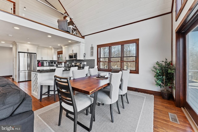 dining space with lofted ceiling, light wood-style flooring, baseboards, and visible vents