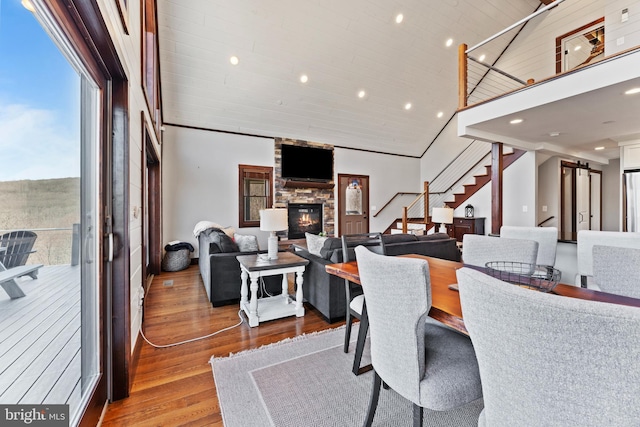 dining area with stairway, a barn door, a fireplace, wood finished floors, and high vaulted ceiling