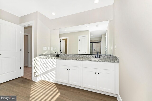 bathroom with double vanity, wood finished floors, a sink, and a shower stall