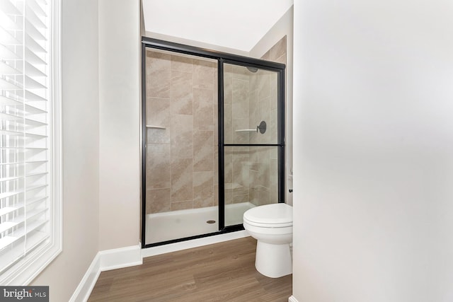 bathroom with a stall shower, baseboards, toilet, and wood finished floors