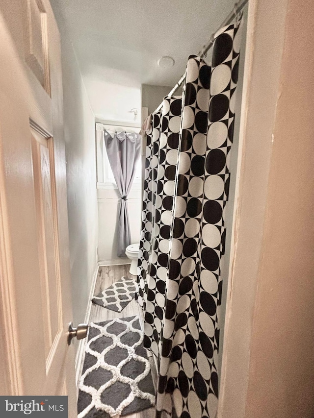 full bathroom with toilet, a shower with curtain, and wood finished floors