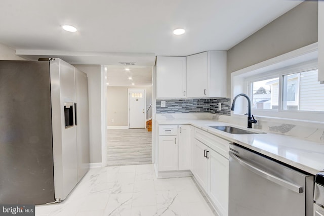 kitchen featuring white cabinets, appliances with stainless steel finishes, a sink, marble finish floor, and backsplash