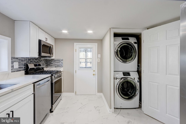 kitchen featuring decorative backsplash, white cabinets, appliances with stainless steel finishes, stacked washer / drying machine, and marble finish floor