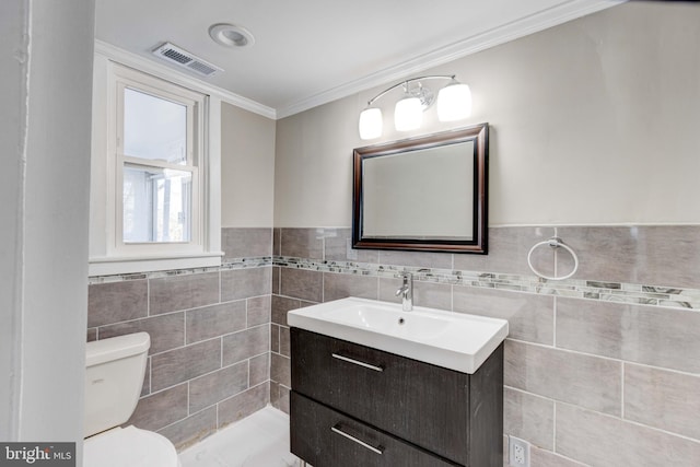 bathroom with tile walls, visible vents, toilet, ornamental molding, and vanity