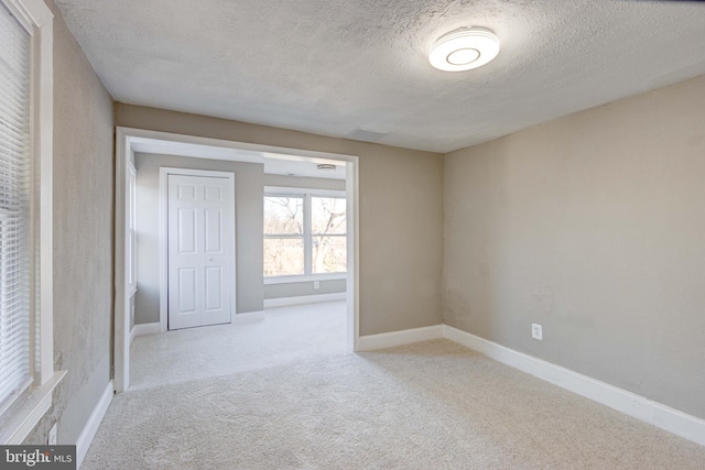 carpeted spare room with a textured ceiling and baseboards