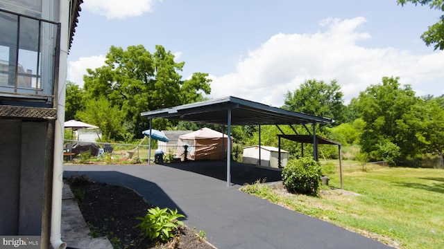 view of vehicle parking featuring aphalt driveway, a detached carport, and fence