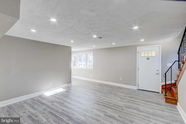 below grade area with light wood-type flooring, stairs, and a textured ceiling