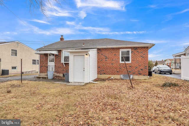 rear view of property featuring brick siding, a yard, a chimney, and central AC unit