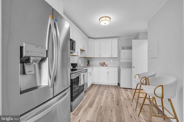 kitchen with ornamental molding, appliances with stainless steel finishes, stacked washer and clothes dryer, and white cabinets