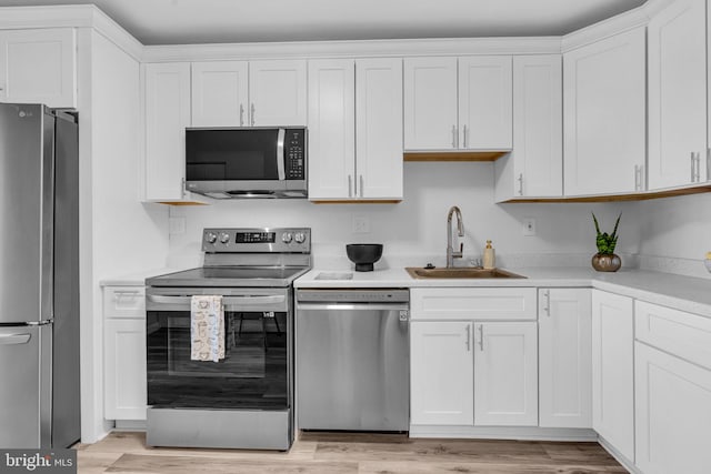 kitchen with appliances with stainless steel finishes, light wood-style floors, white cabinets, and a sink