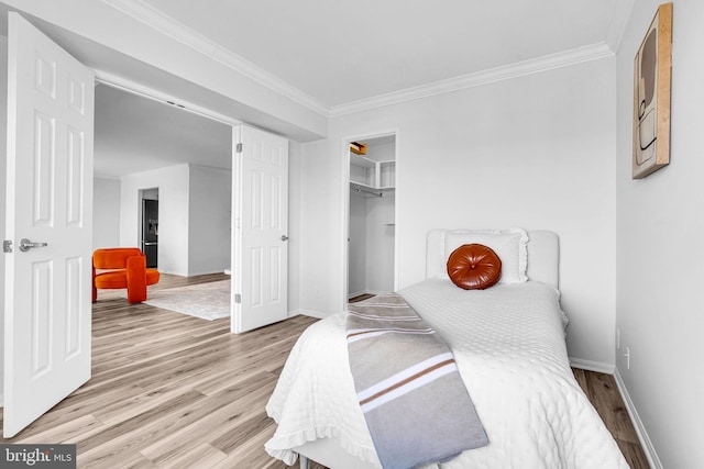 bedroom with a walk in closet, crown molding, a closet, wood finished floors, and baseboards