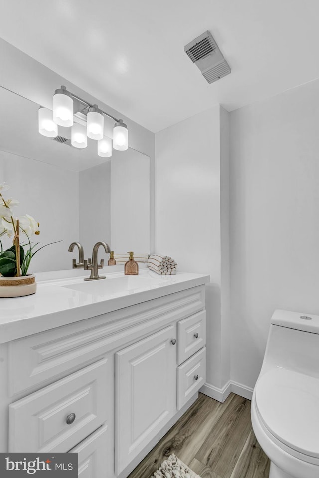 bathroom with baseboards, visible vents, toilet, wood finished floors, and vanity