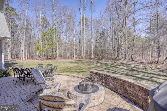 view of patio with outdoor dining space, an outdoor fire pit, and a wooded view