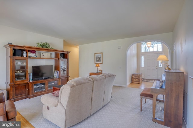 living room with arched walkways, light colored carpet, and baseboards