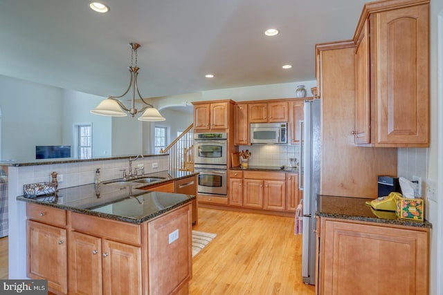 kitchen featuring a kitchen island with sink, a sink, appliances with stainless steel finishes, decorative backsplash, and light wood finished floors