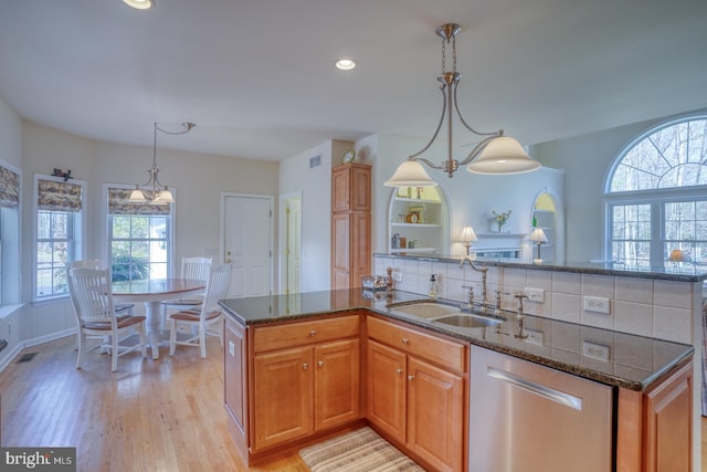 kitchen with a sink, light wood-type flooring, decorative backsplash, dishwasher, and dark stone countertops